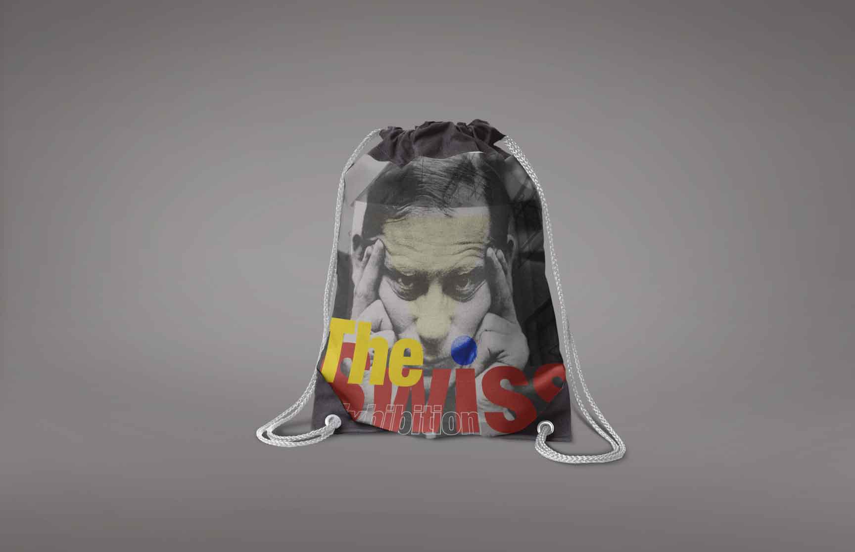 A drawstring bag featuring a Swiss-style design with a grayscale portrait of a man holding his head, overlaid with bold typography reading ‘The Swiss Exhibition’ in red and yellow, accented by geometric elements such as a blue circle. The bag emphasizes minimalism and structured aesthetics.